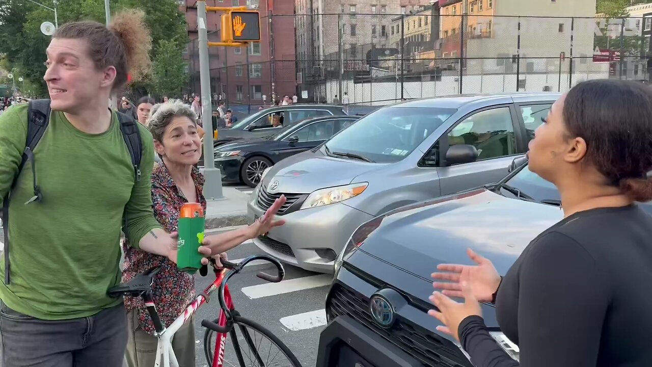 In NYC, two white liberals obstructing traffic, laugh at a black woman attempting to get to her job.