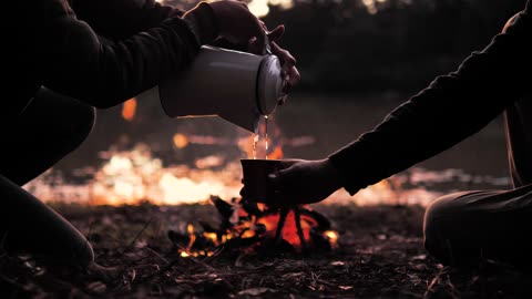 People pouring a warm drink around a campfire